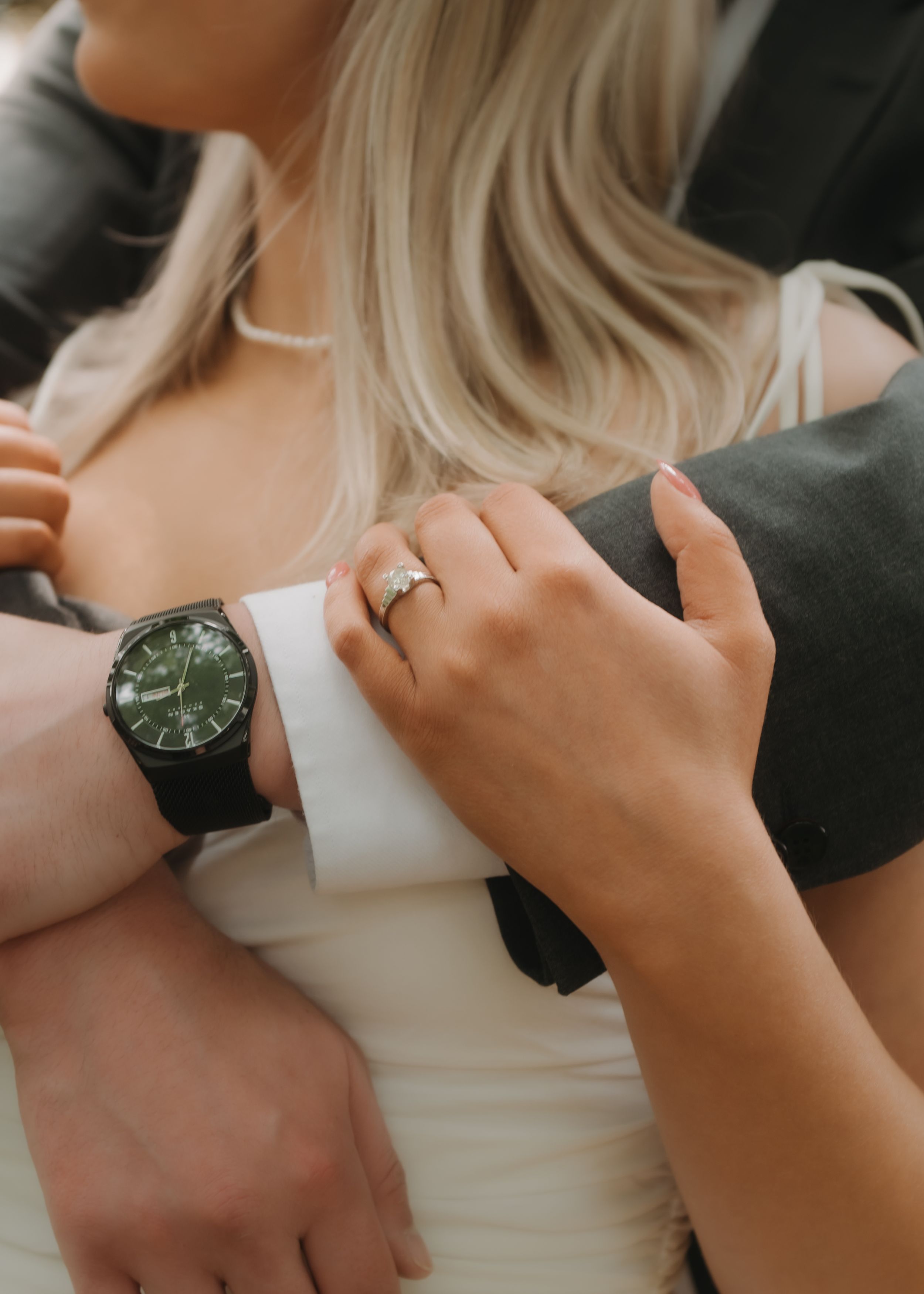 Close-up shot showing hands with a wedding ring and black watch against white fabric in an intimate embrace.