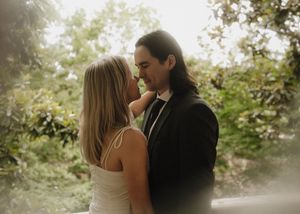 A romantic couple shares a tender moment in a dreamy garden setting with soft backlit sunlight filtering through trees.
