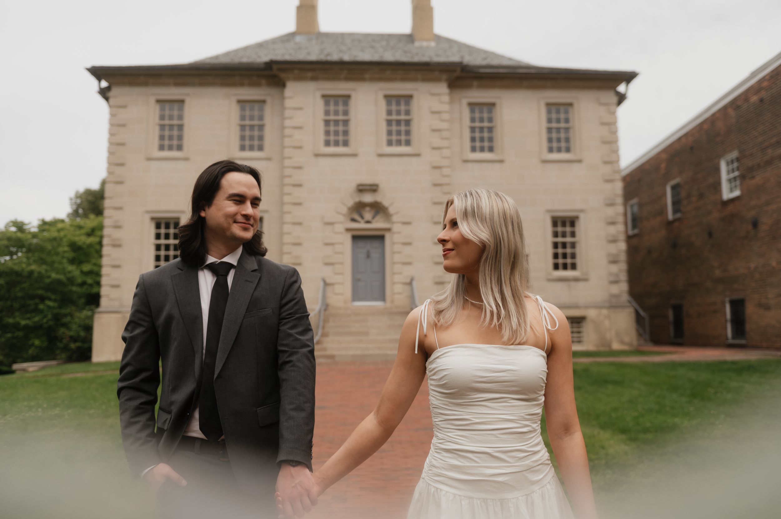 A wedding couple laughs and walks together outside a historic stone building on their special day.
