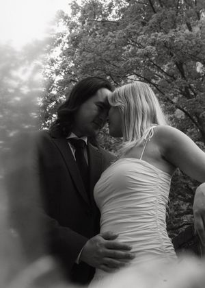 A romantic black and white portrait of a couple embracing outdoors with trees in the background.