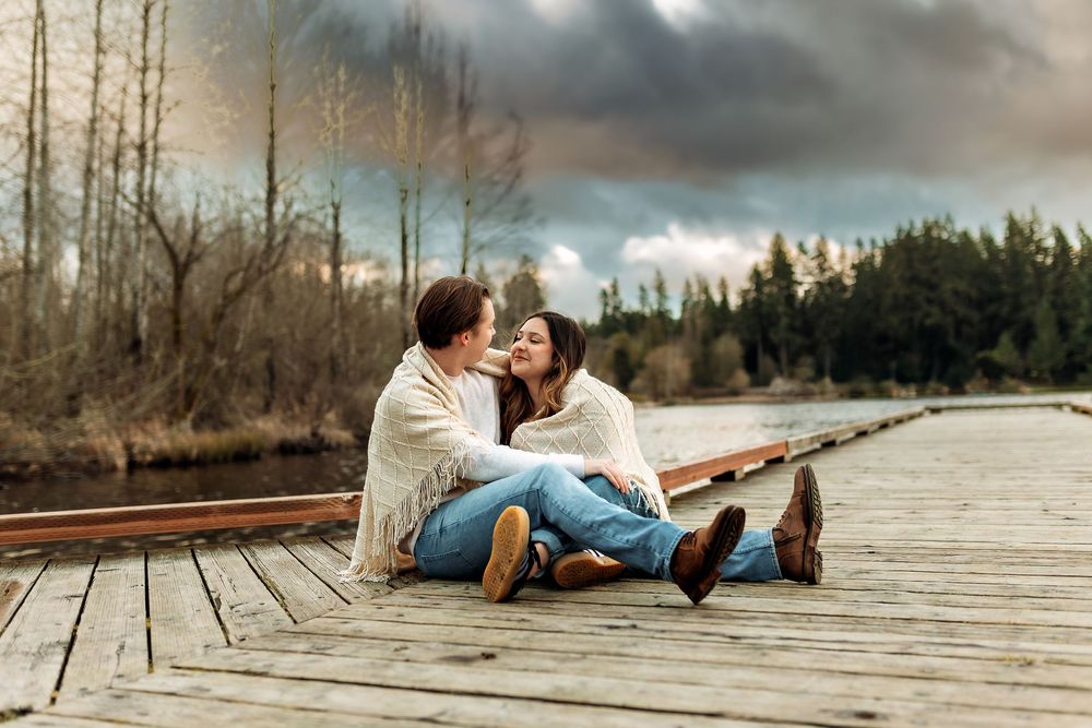 Couple relaxing on wooden dock with dramatic sunset and lake views.