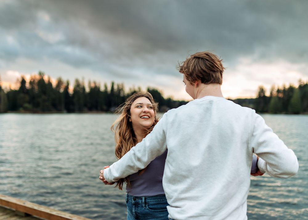 Couple walking hand in hand on lakeside dock during golden hour.