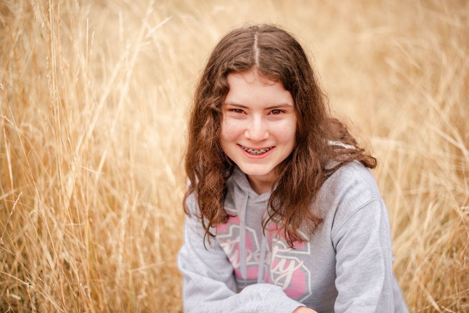 Someone sitting in a golden wheat field wearing a gray sweatshirt on a sunny autumn day.