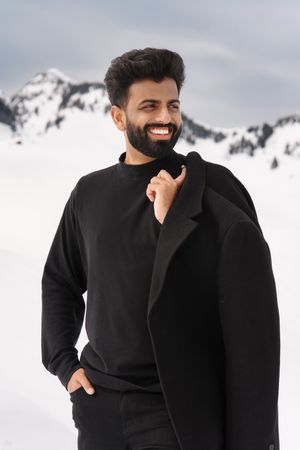 Person wearing a black sweater laughs joyfully against a snowy mountain backdrop.