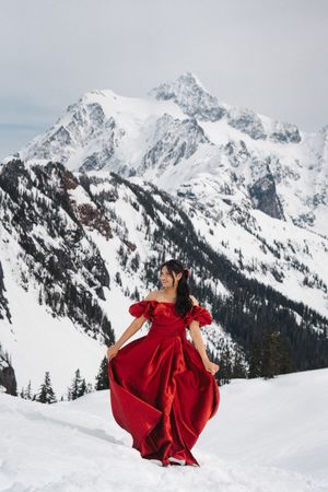 A flowing red dress billows dramatically against snowy mountain peaks in Washington's winter landscape.
