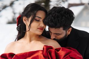 A romantic winter photo shoot in the snow with two people in red attire against snowy mountain backdrop.