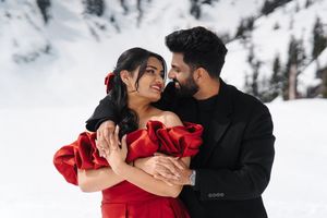 A couple in winter attire share romantic moments in a snowy landscape setting while wearing red and black clothing.
