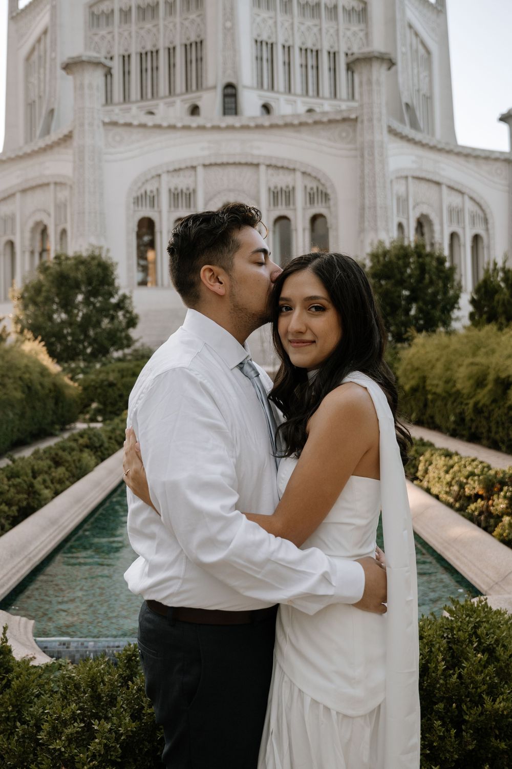 Couple shares intimate moment in front of grand white temple architecture with reflecting pool.