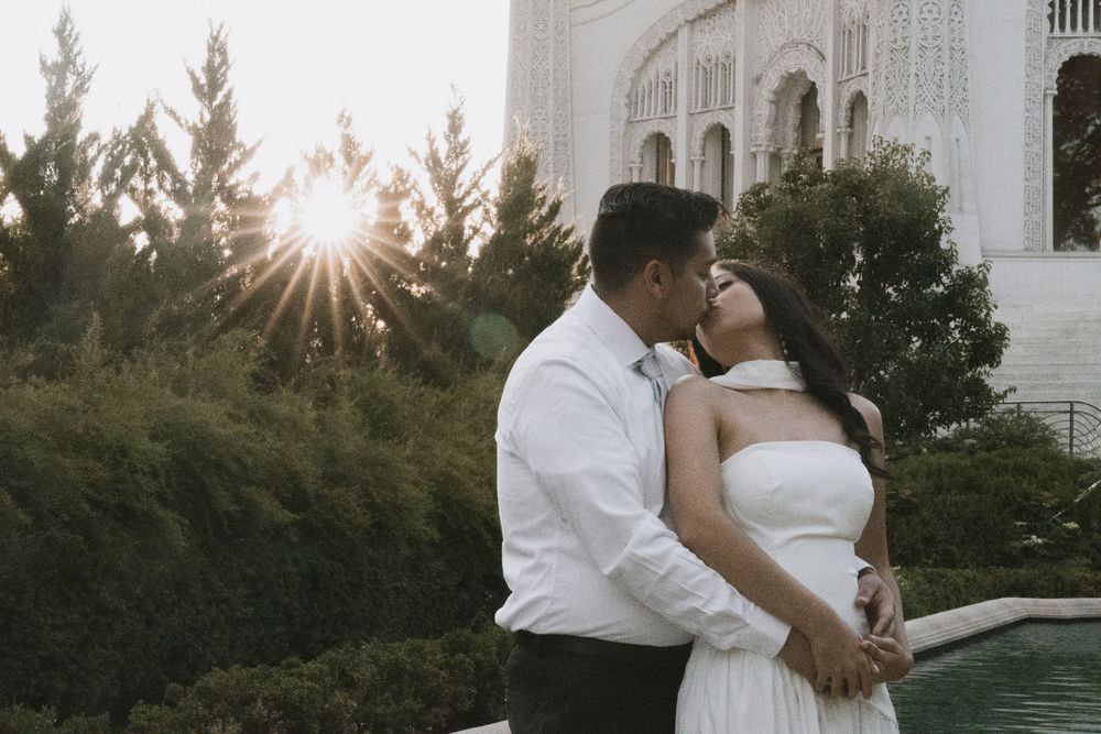 A romantic scene at sunset outside a white classical building with sun rays peeking through trees.