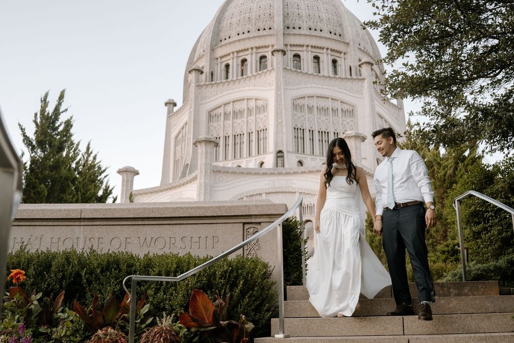 Romantic couple posing on steps of Baha'i Temple with dramatic architectural backdrop.