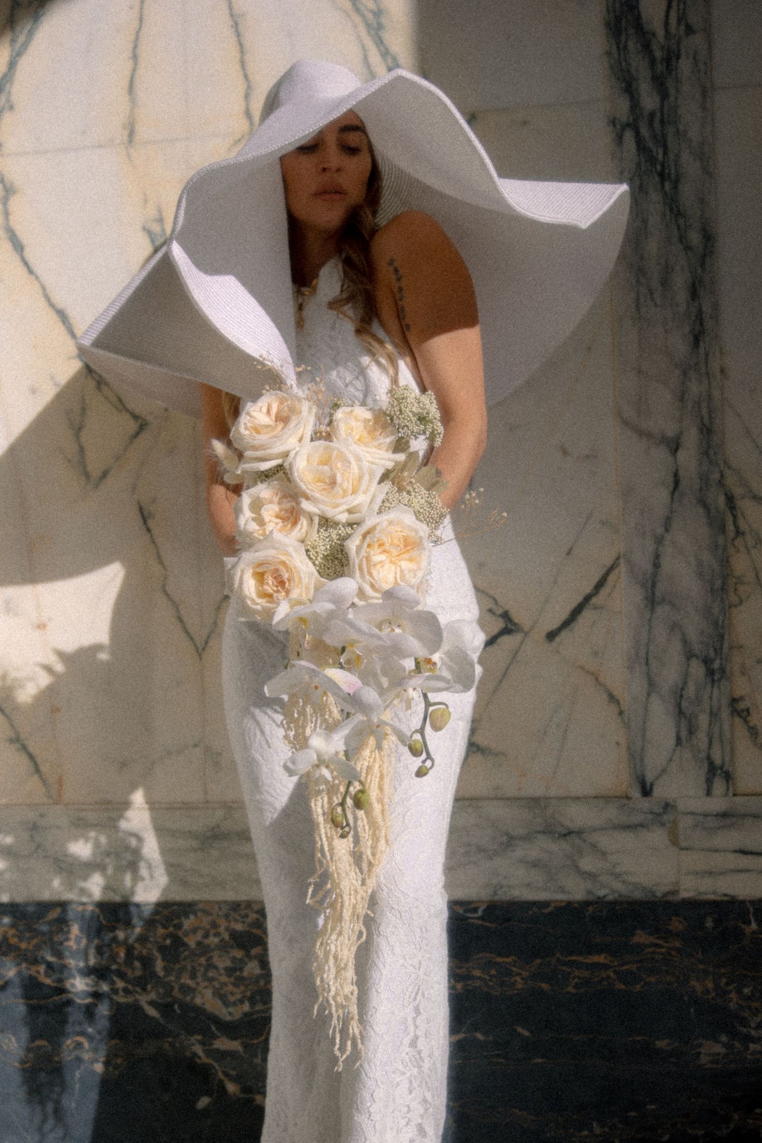 A close-up view of a white bridal gown with lace details and an elegant bouquet of illuminated flowers against a marble wall.
