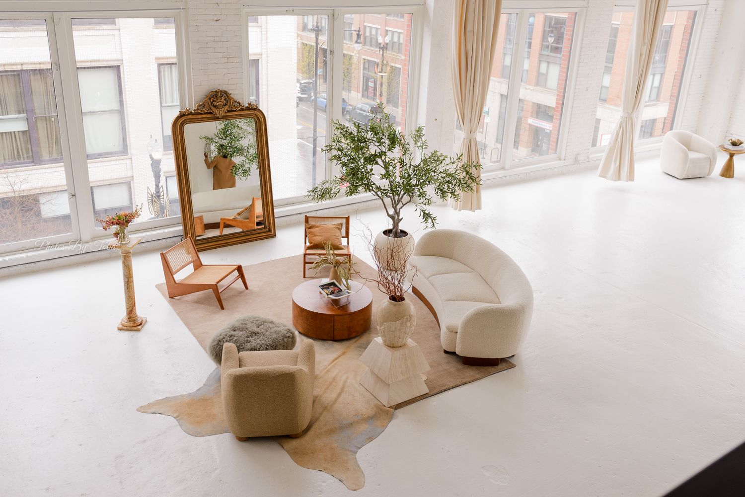 Airy white interior space with large windows, decorative mirrors and potted plants.
