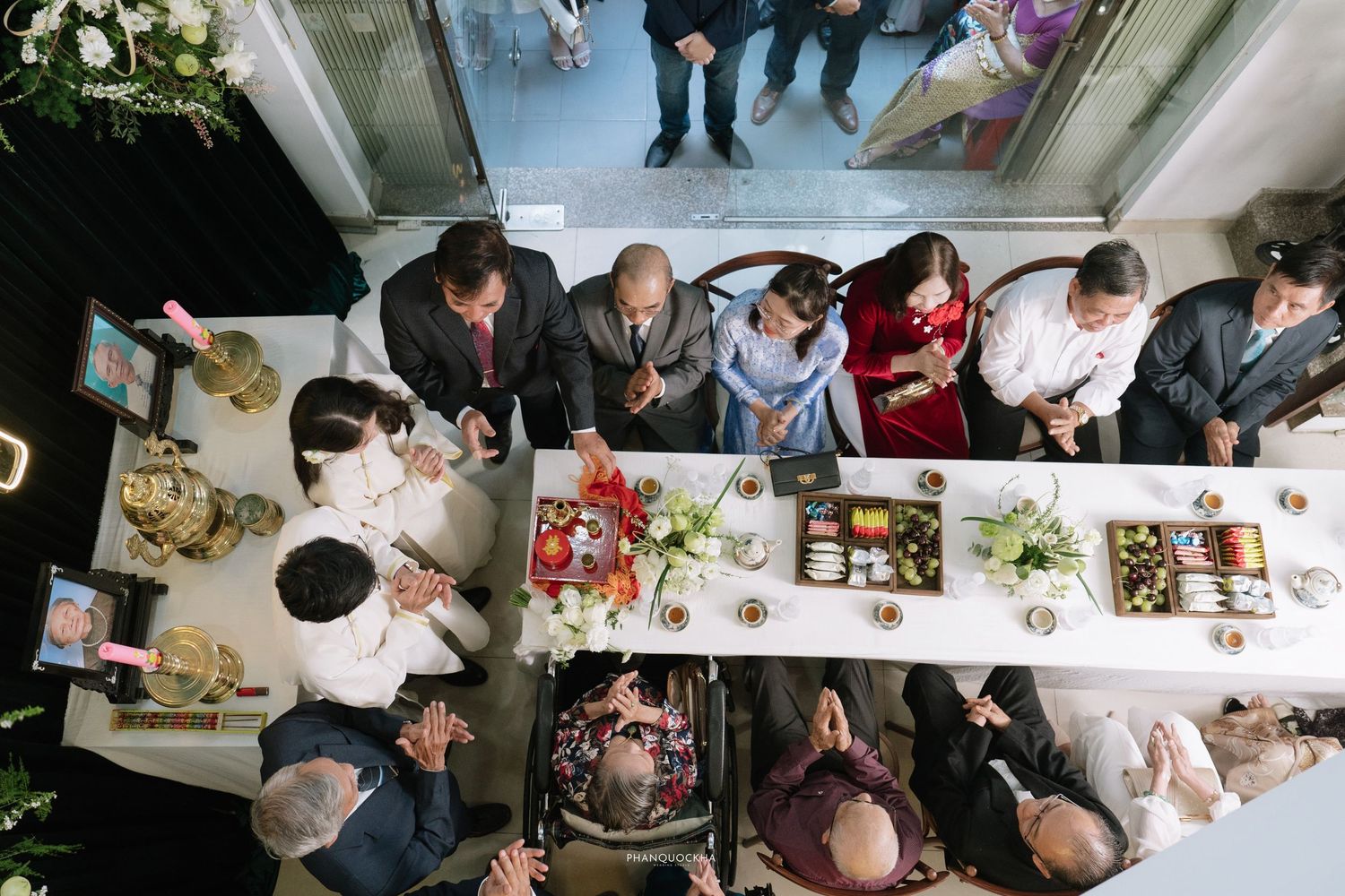 Aerial view of Vietnamese engagement ceremony with guests gathered around a decorated table with traditional offerings.