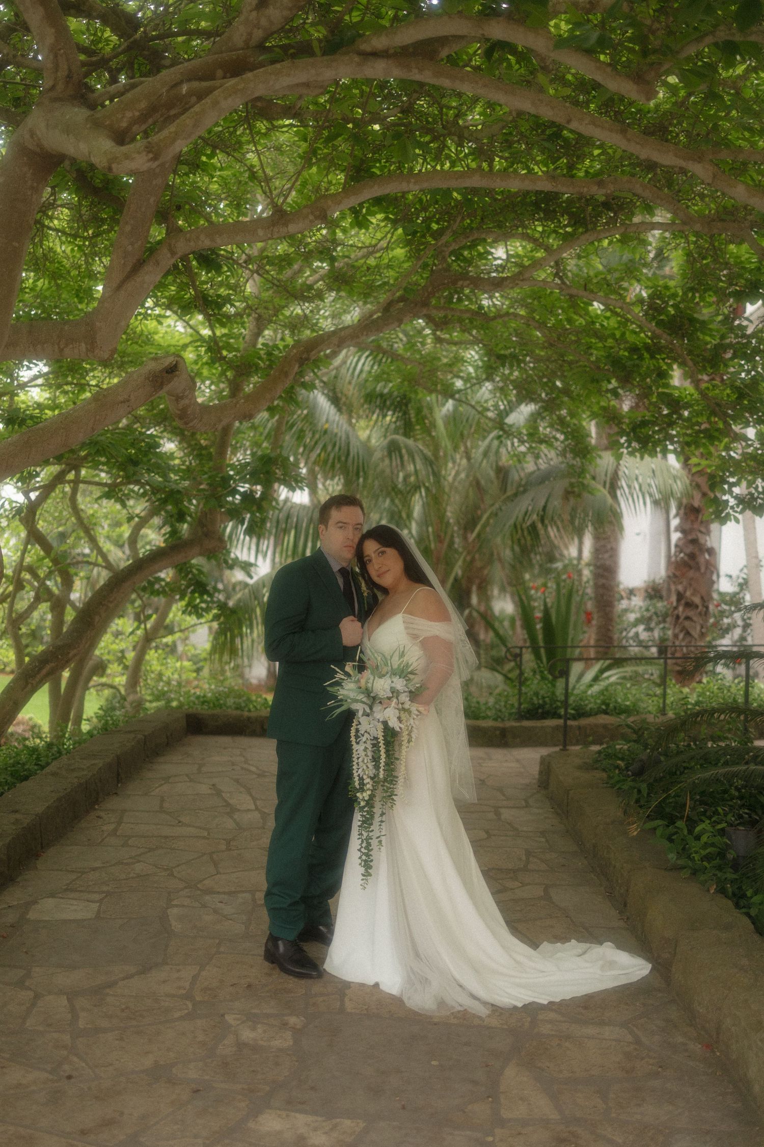 A bride and groom share intimate moments under a canopy of trees in a romantic garden setting.