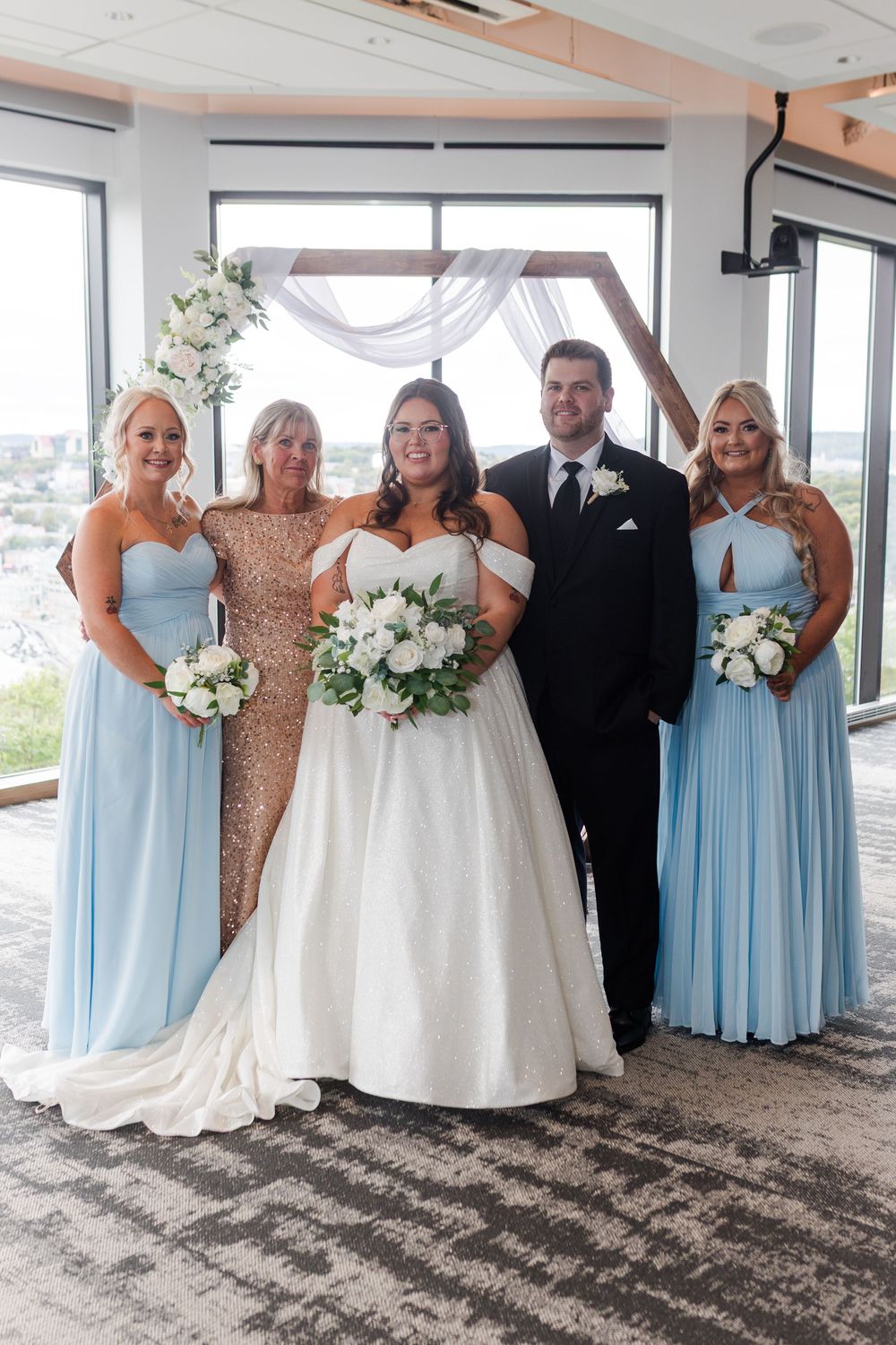 Wedding party in blue bridesmaid dresses and formal attire pose together in an elegant venue with natural lighting.