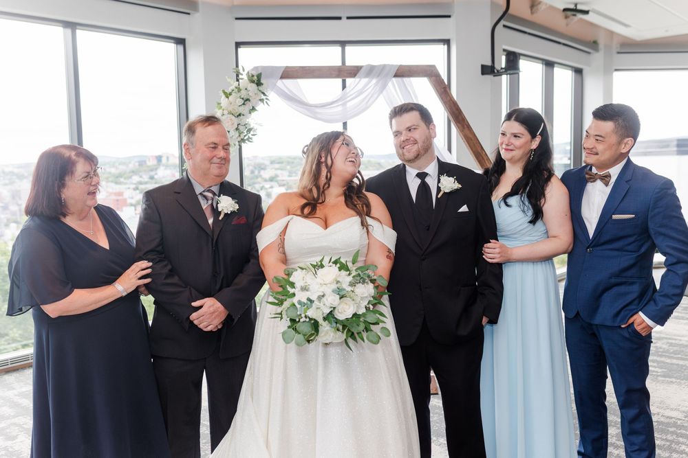 Wedding party in formal attire poses and laughs together in a bright indoor venue for group photos.