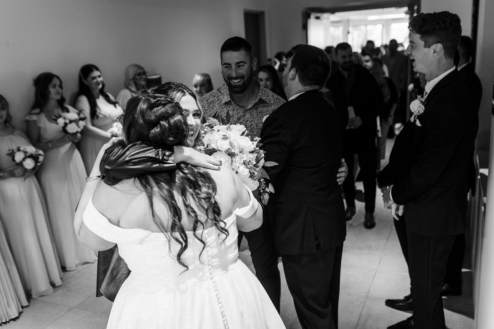A black and white panoramic photo of wedding guests during an emotional reception moment at an indoor venue.