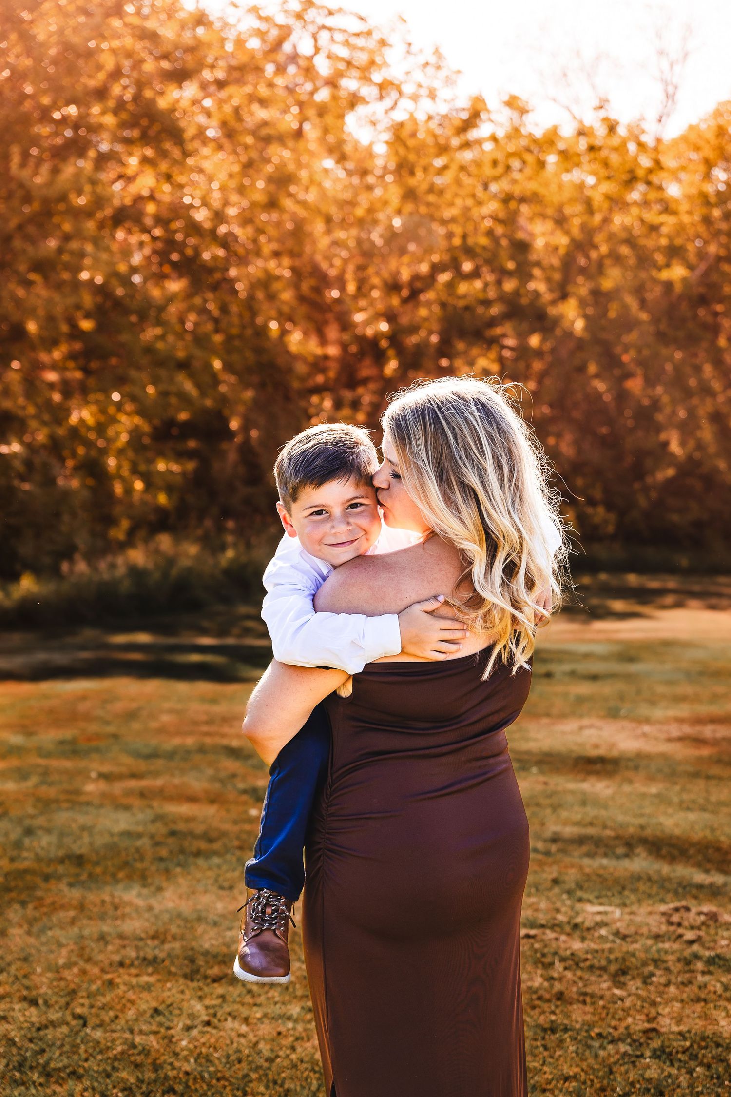 A pair embrace in a warm golden sunset light in an autumn field with trees silhouetted in the background.