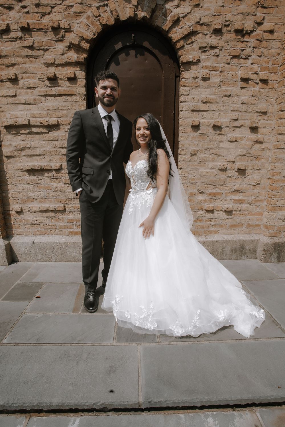 Classic brick wall backdrop frames a romantic wedding portrait shoot with the bride's white lace gown flowing elegantly.