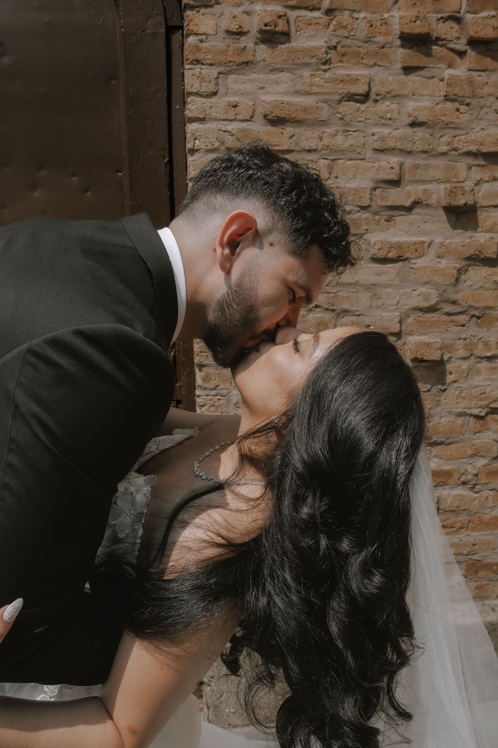 A romantic wedding portrait sequence against a brick wall shows the couple sharing an intimate kiss.