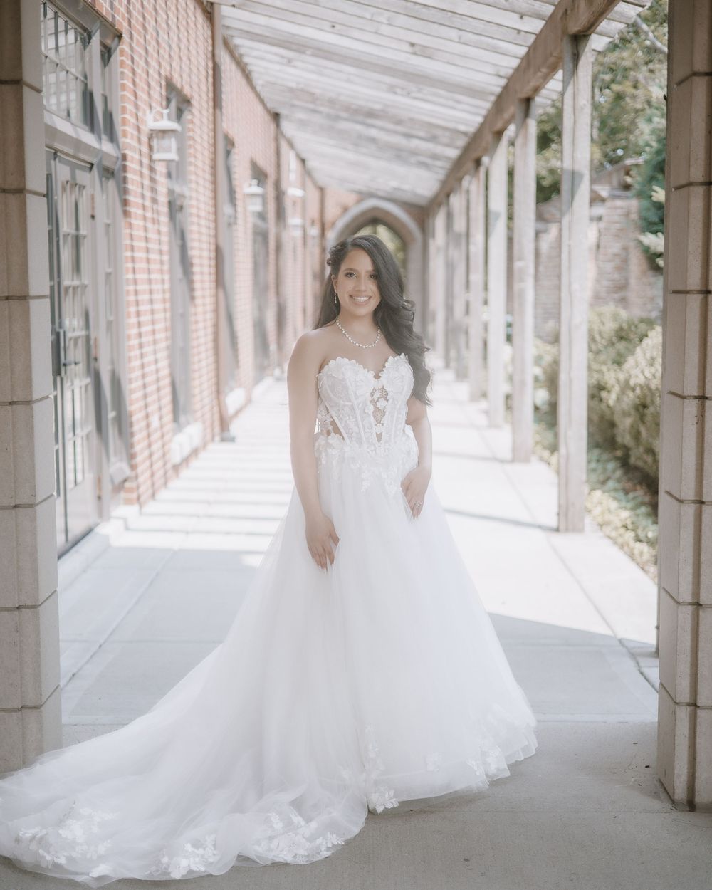 Elegant wedding dress with flowing tulle skirt photographed in a sunlit covered walkway.