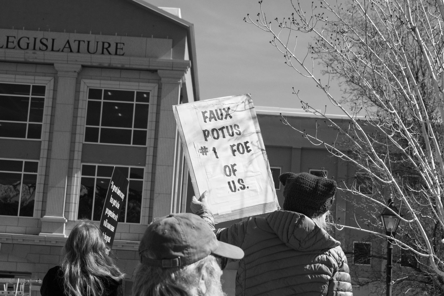 Protester holds Faux POTUS #1 Foe of U.S. sign outside a building marked Legislature.
