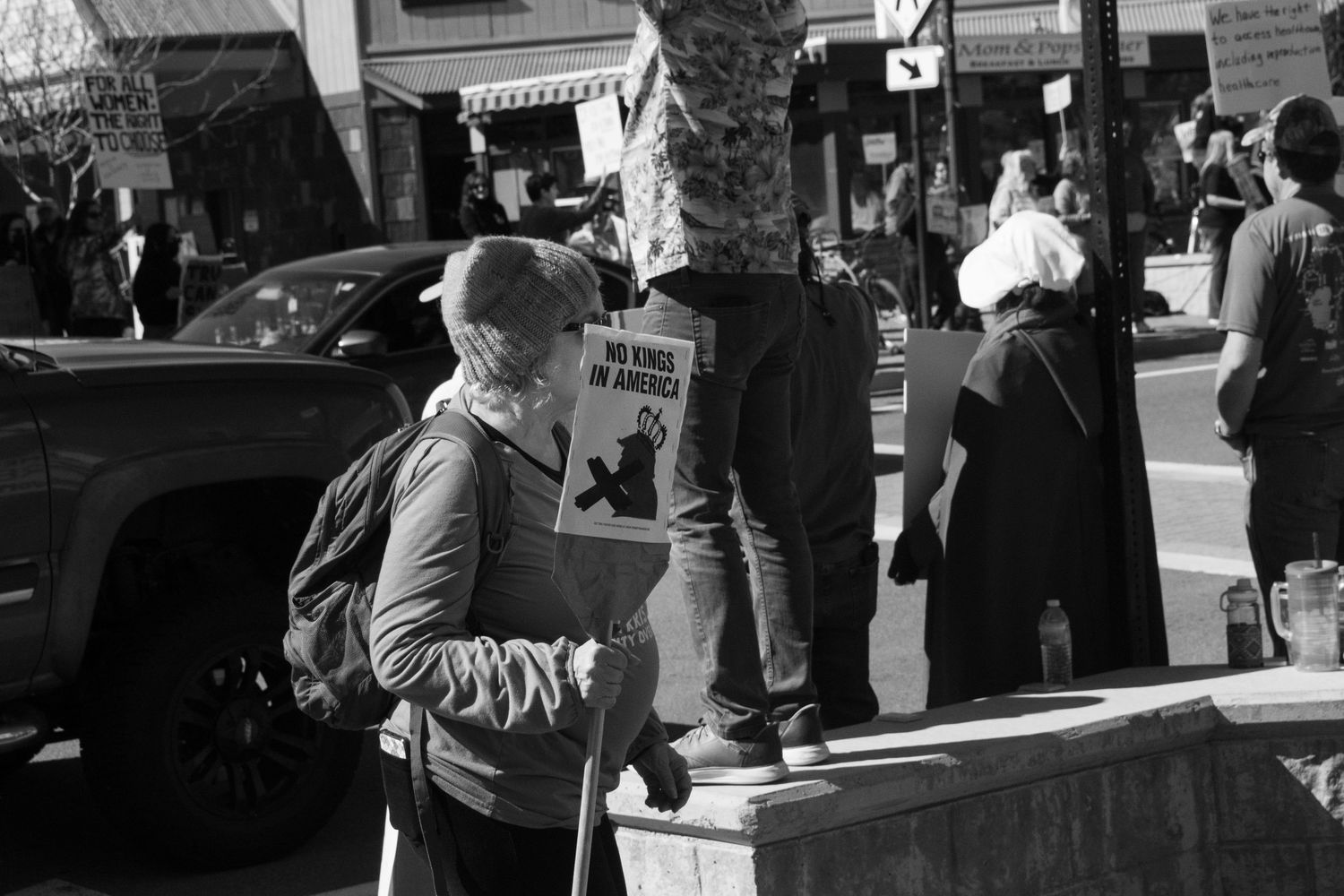 Black and white street photo of a person holding a protest sign on a busy urban sidewalk.