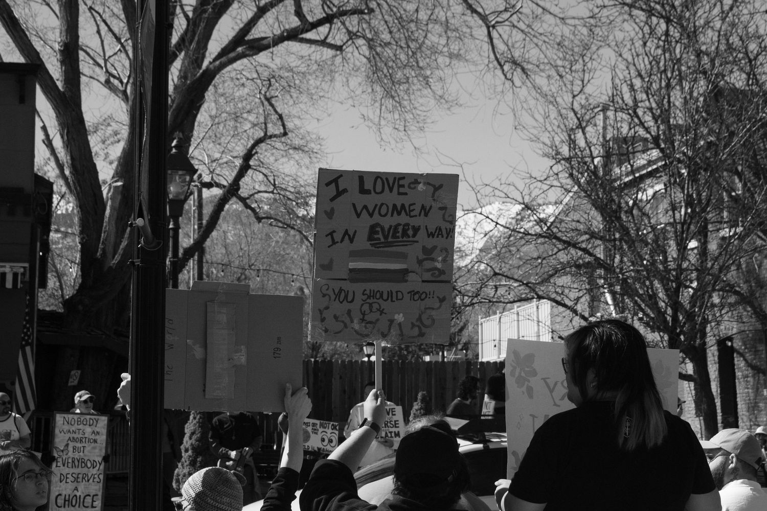 Crowd of protesters holding signs at an outdoor rally, with a visible sign reading I Love Women in Every direction.