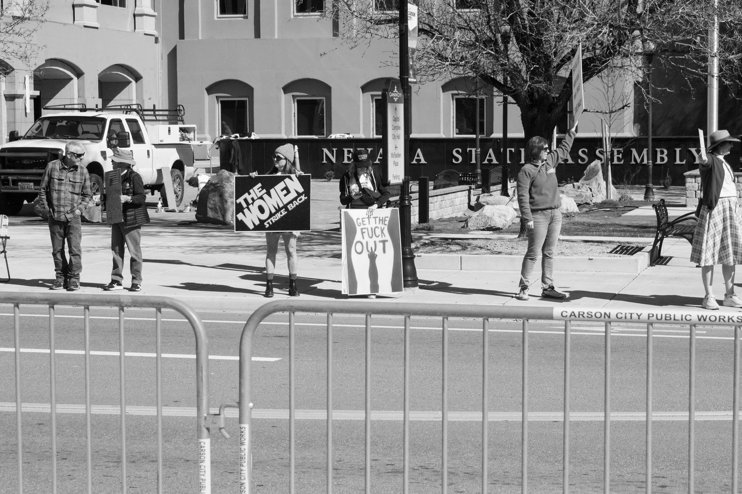 Small group of protesters with signs stand outside the Nevada State Assembly building behind metal barricades.