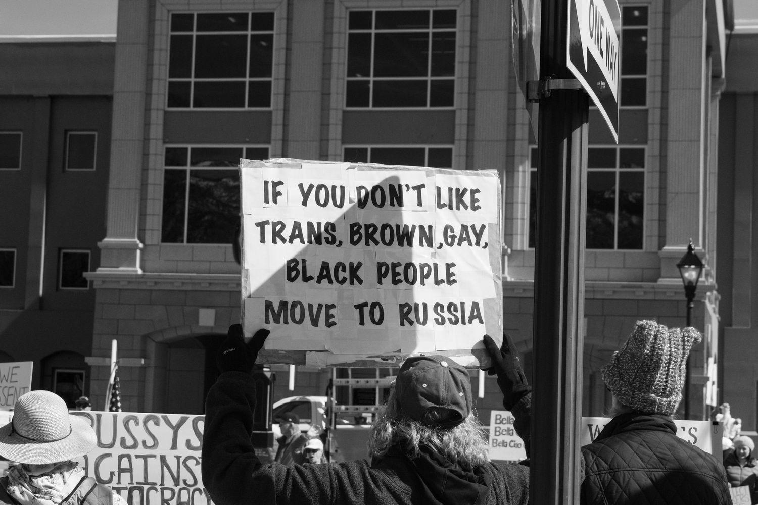Protester holds sign reading If You Dont Like Trans Brown Gay Black People Move To Russia at rally.