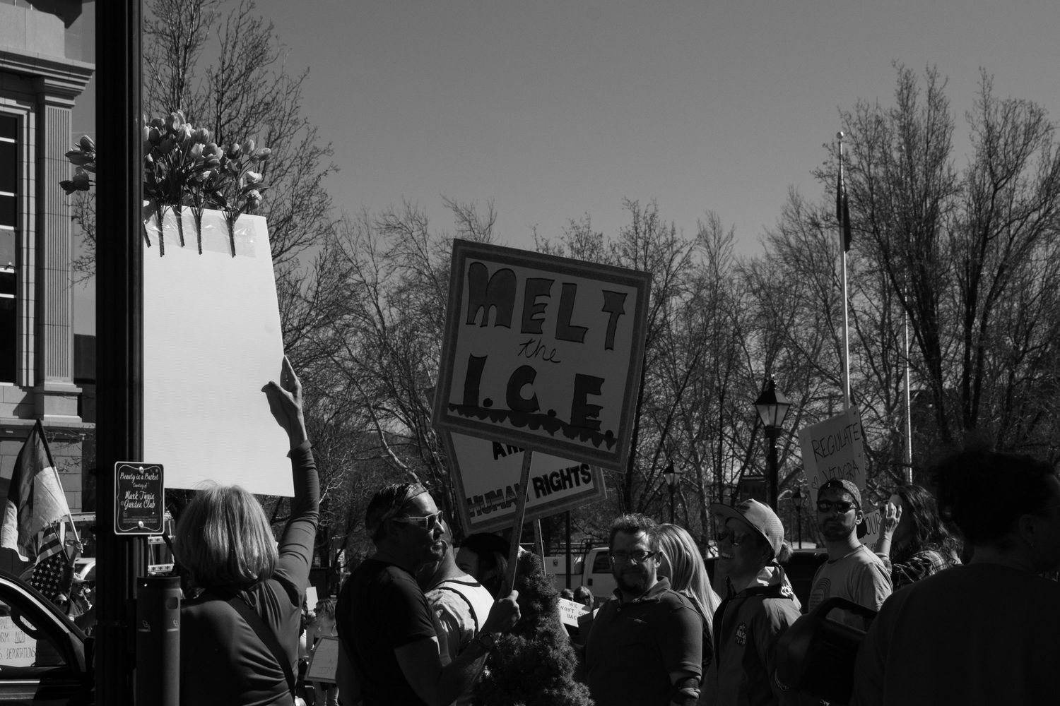 Black and white photo of protesters holding signs including Melt ICE at an outdoor rally.