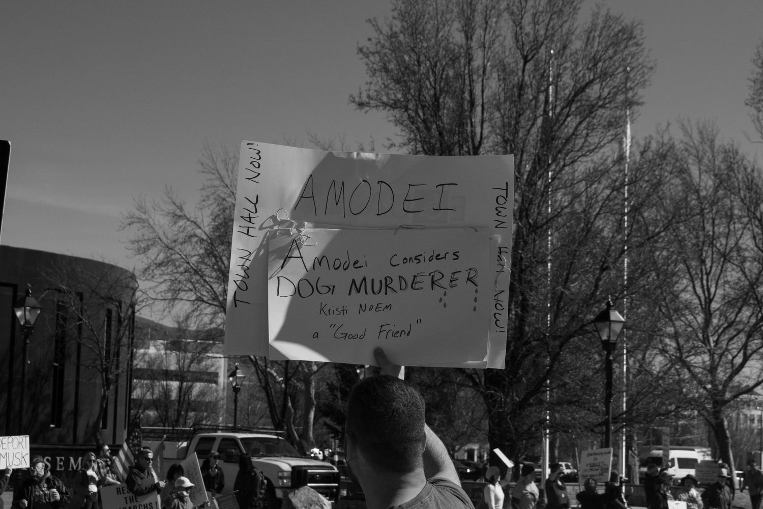 Black and white protest photo featuring a sign reading Amodei Dog Murderer at a public demonstration.