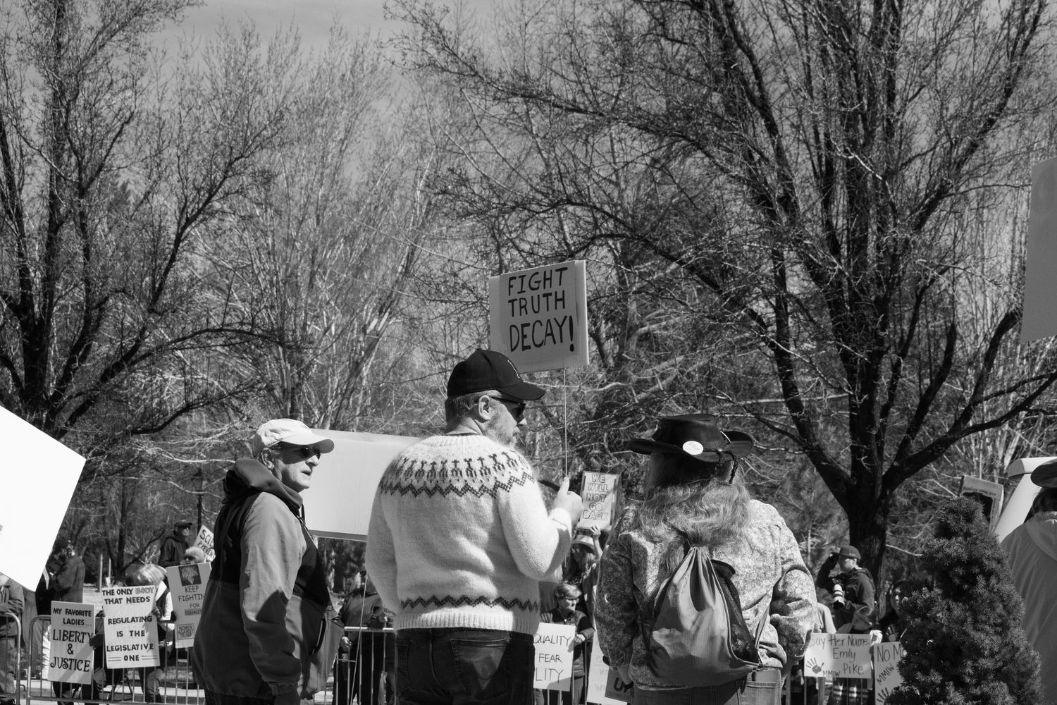 Black and white photo of protesters gathered among bare trees holding various demonstration signs.