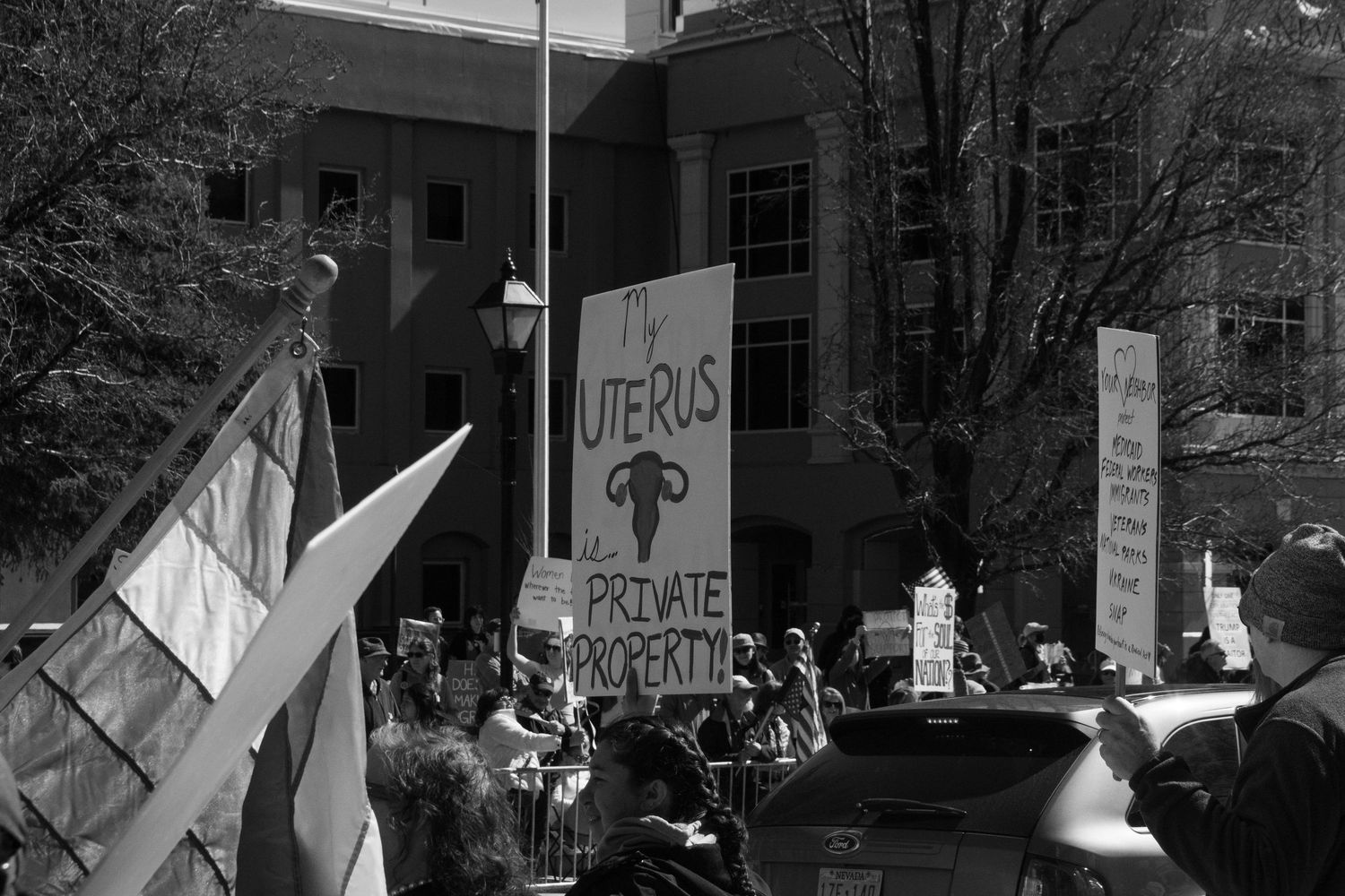 Black and white photo of protest with sign reading My Uterus is Private Property at outdoor rally.