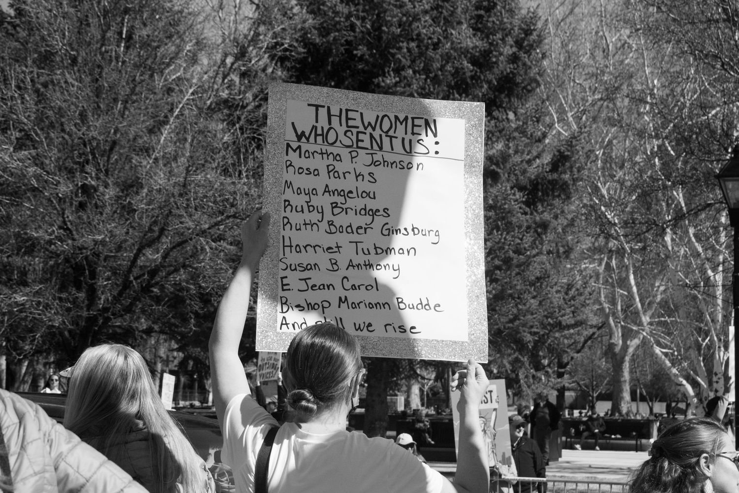 Protester holds sign listing influential women including Ruth Bader Ginsburg at outdoor rally.