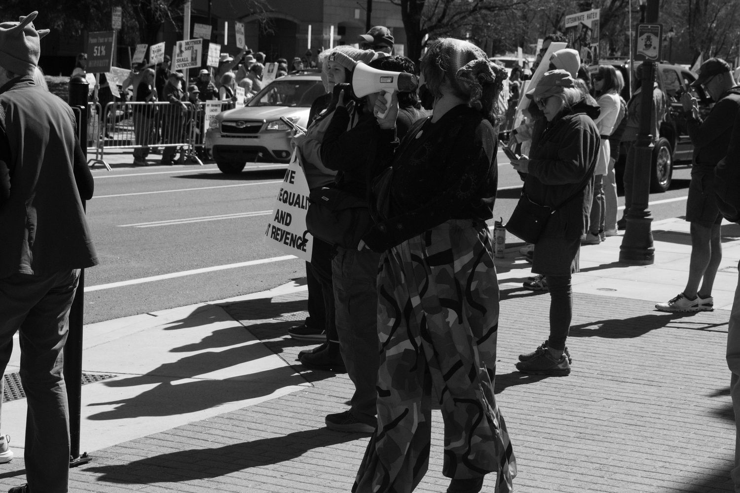 Black and white photo of protesters on urban sidewalk with megaphone at street demonstration.