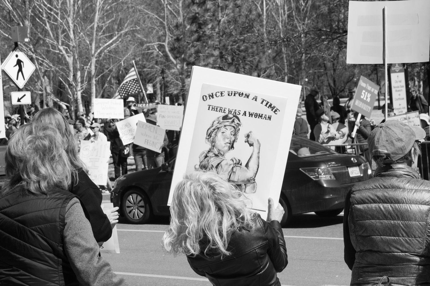 Black and white image of protesters marching with a sign reading Once Upon A Time There Was A Woman at an outdoor rally.