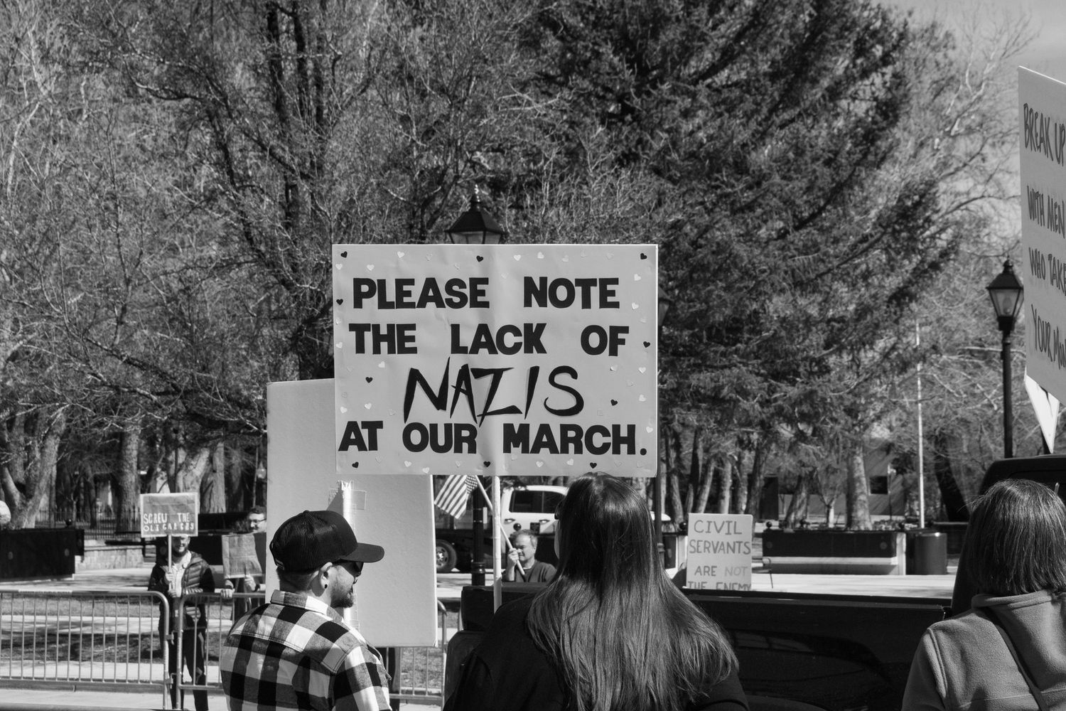 Black and white protest photo featuring a sign reading Please Note The Lack Of Nazis At Our March held by a demonstrator.