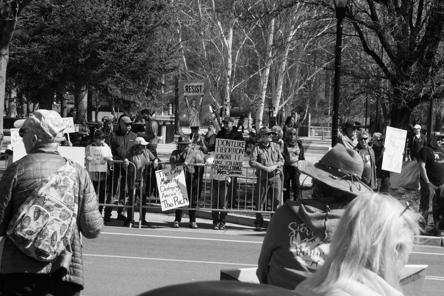 Crowd of protesters holding signs behind metal barricades at an outdoor political rally.