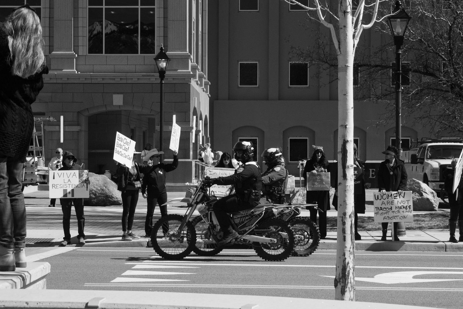 Black and white photo of a police officer on motorcycle passing protesters holding signs at a rally.