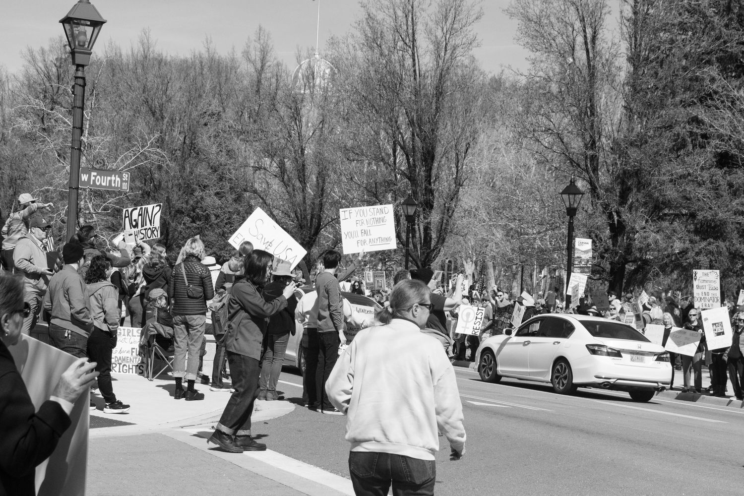 Black and white image of protesters lining a street holding signs during a public rally.