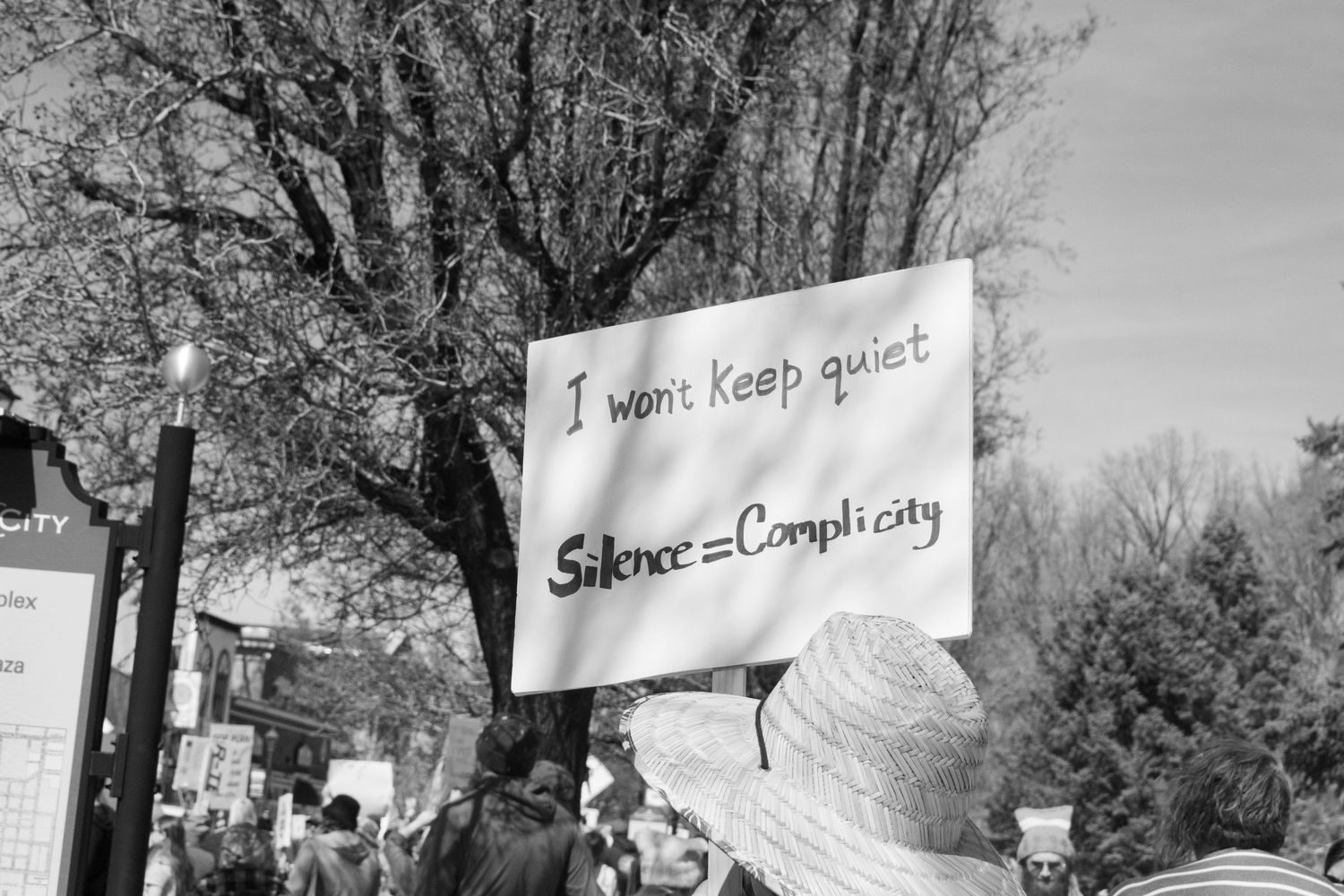 Protester holds sign reading I Wont Keep Quiet Silence Equals Complicity at outdoor rally.