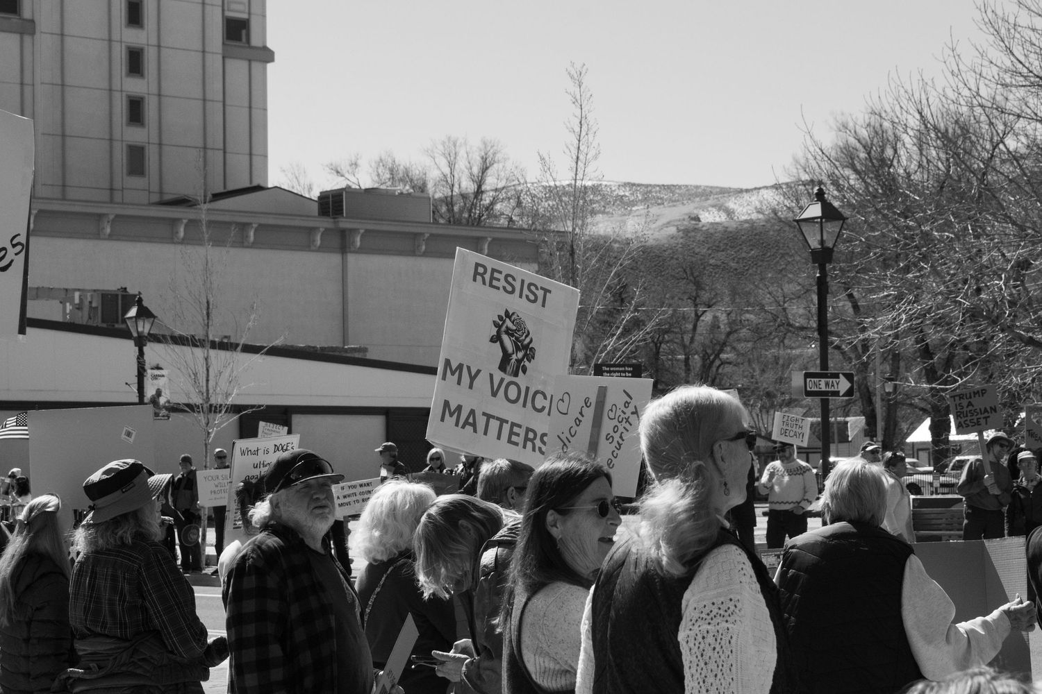 Black and white image of protesters holding resist and my voice matters signs at a public demonstration.