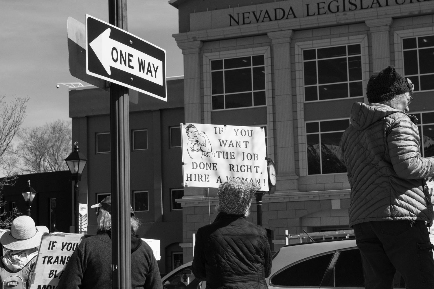 Black and white photo outside Nevada Legislature with sign reading If You Want The Job Done Right Hire A Woman.