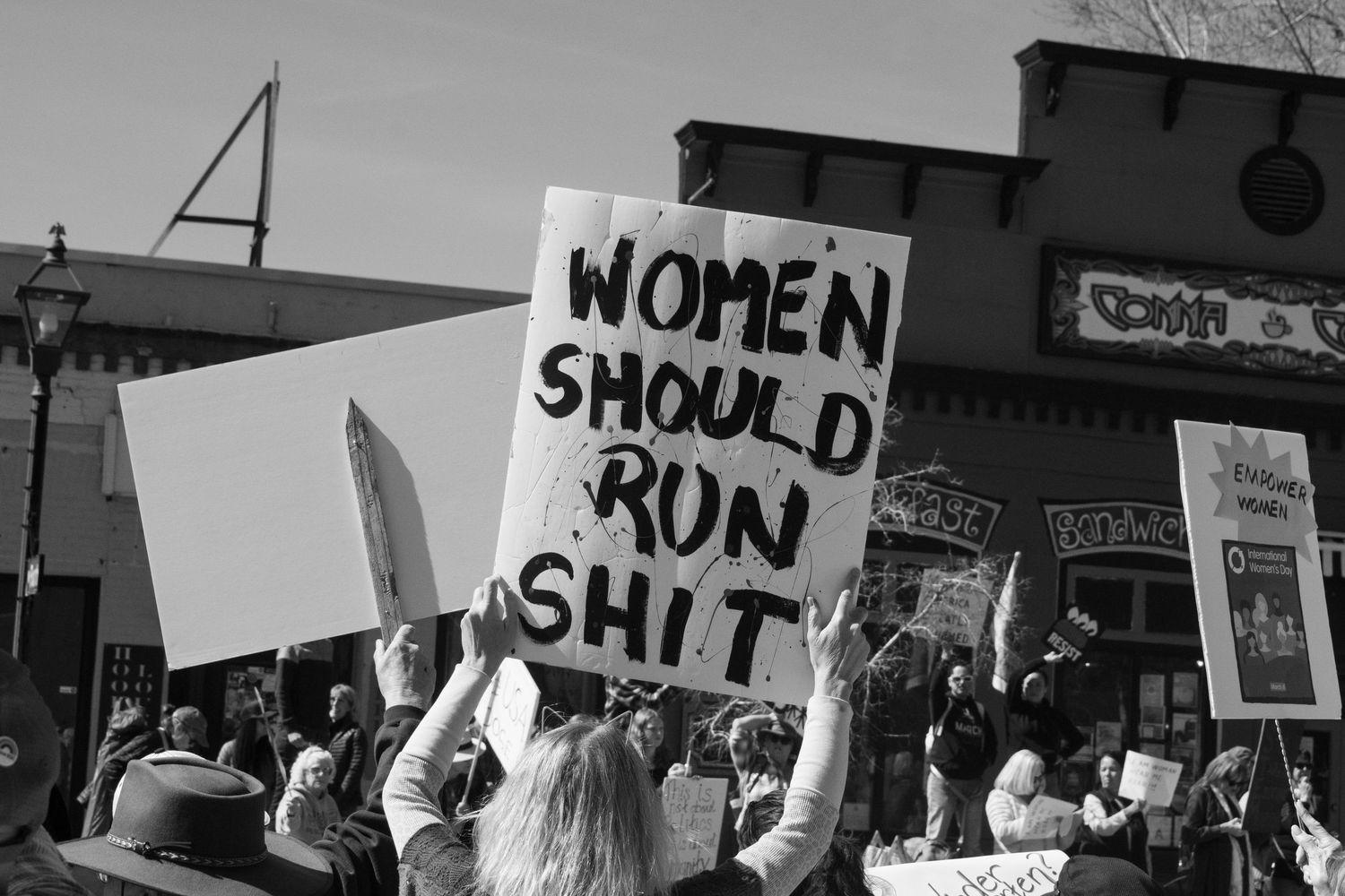Black and white photo of crowd holding women should run shit sign at a political protest rally.
