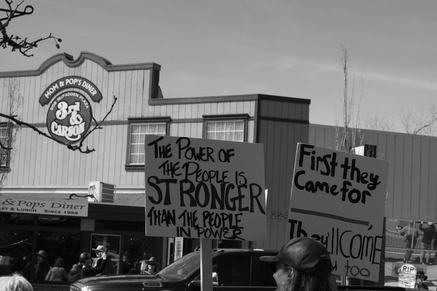 Black and white protest photo with signs reading the power of the people is stronger than the people in power.