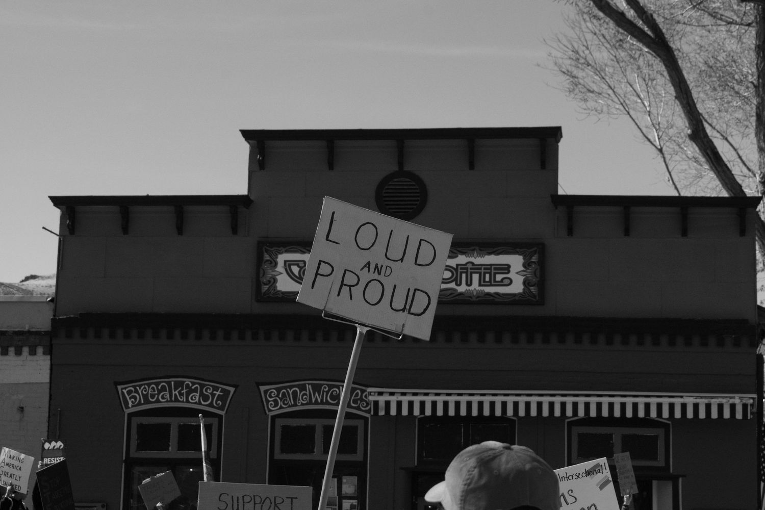 Black and white image of a loud and proud protest sign held above a crowd at a public demonstration.