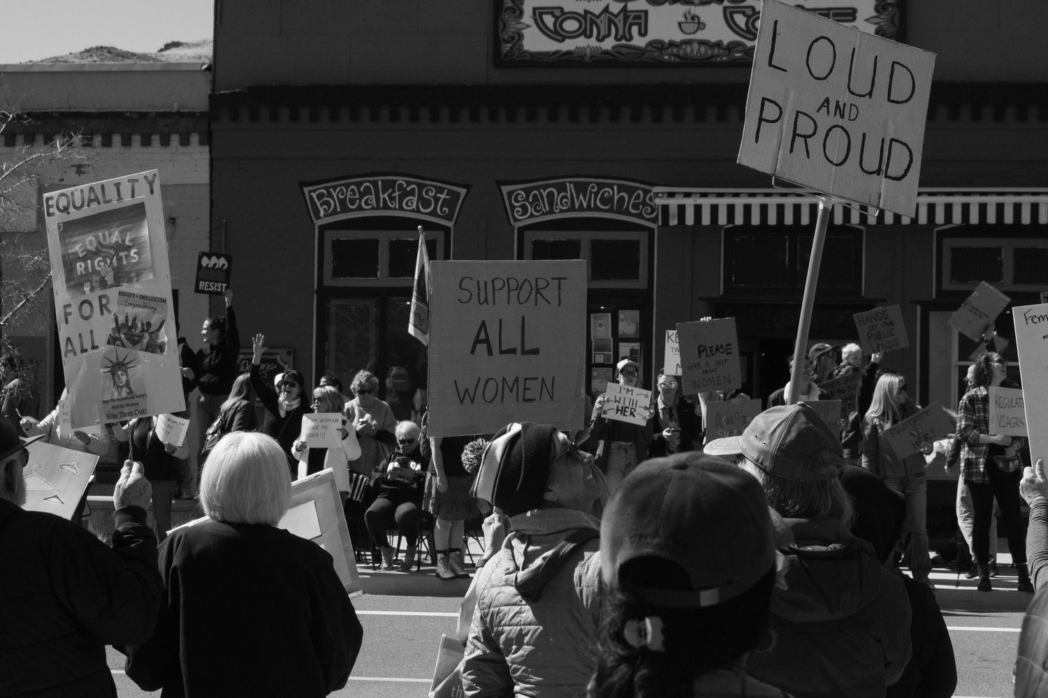 Black and white protest photo featuring support all women and loud and proud signs at a street rally.