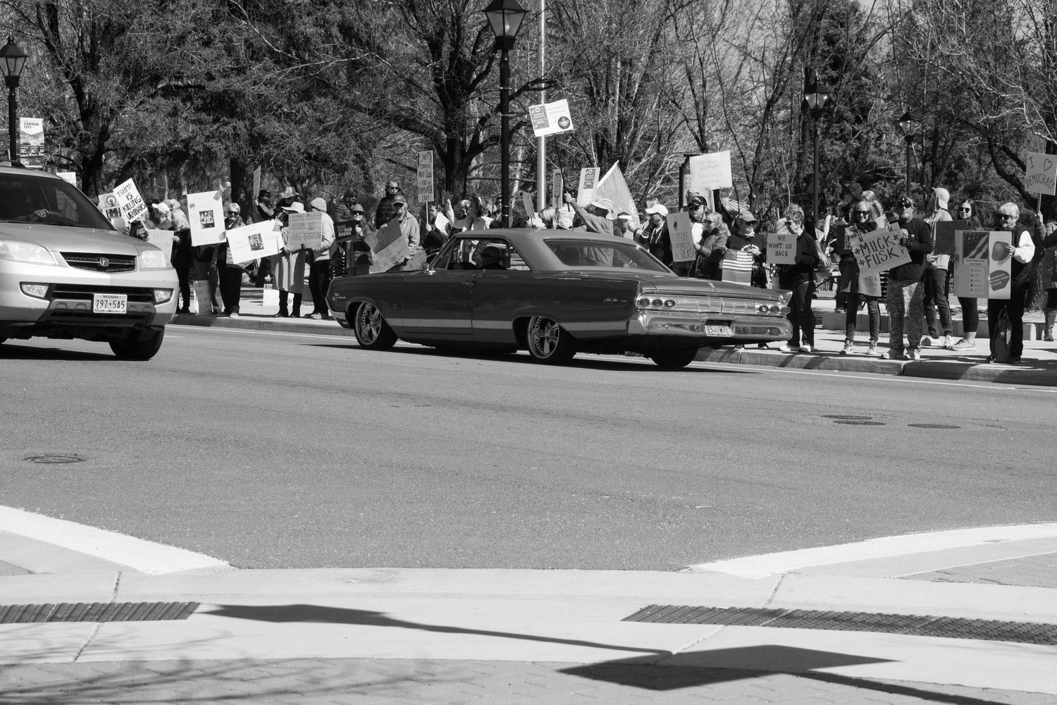 Black and white photo of protesters lining a street holding signs while cars pass during a rally.