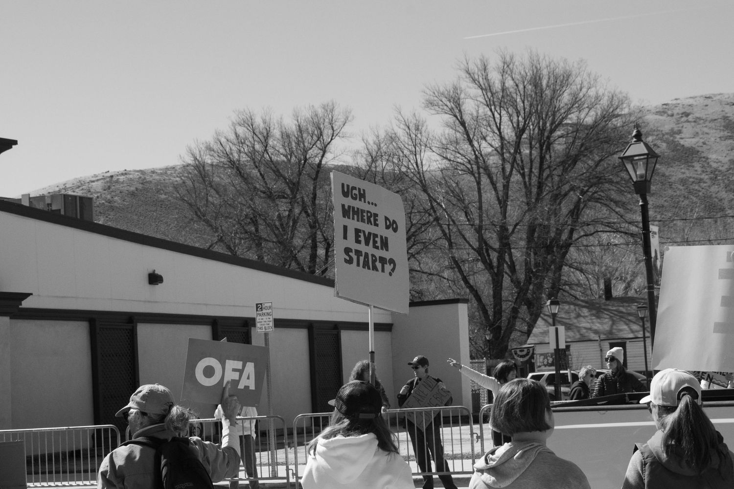 Black and white photo of protesters with OFA banner and humorous handwritten sign at a public rally.